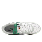 White Air Force 1 with exposed tongue, white laces, green tag, and navy heel accents.