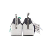 Pair of white sneakers with black heel panels and green pull tab