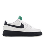 Low-top sneaker with black swoosh on white upper, green lace tag, black sole.