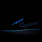 Dark low-top sneaker with glowing blue swoosh detail and blue-tinged laces