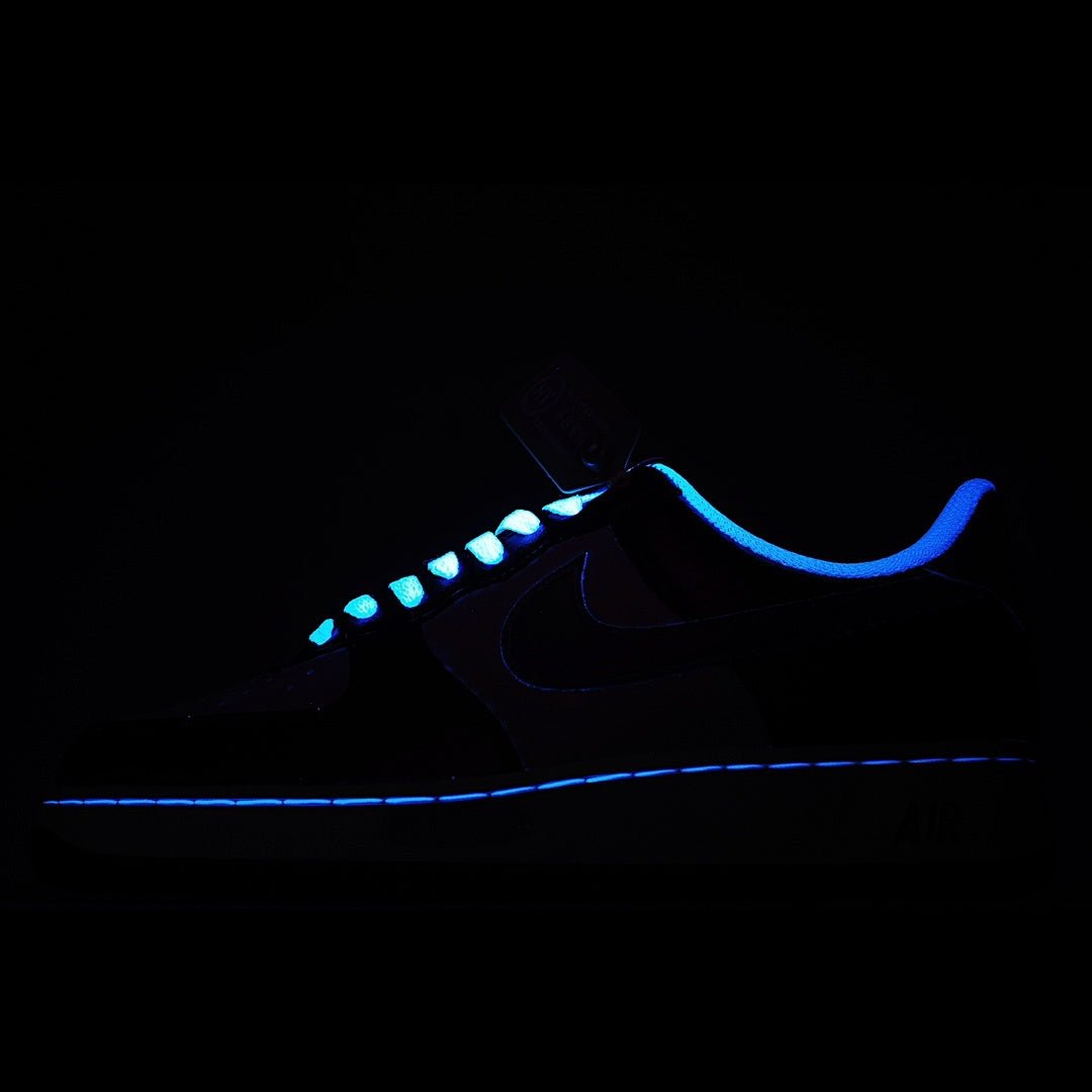 Low-top sneaker in dark lighting, black upper with blue trim and visible swoosh.