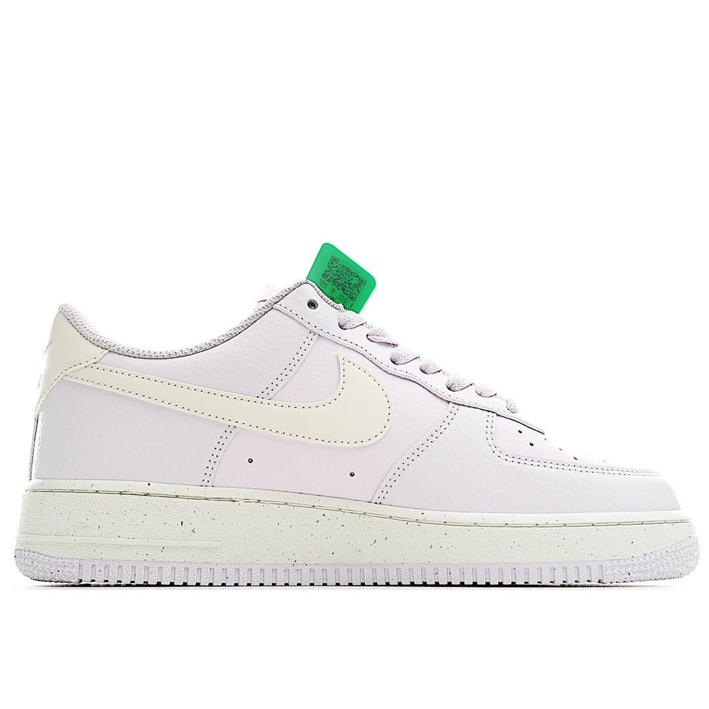 White low-top sneakers with pale yellow swoosh and green tag on tongue