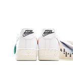 White low-top sneakers with black Nike heel text, speckled sole, teal lace accents
