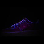 Dark low-top sneakers with purple accent stitching and glowing purple lace area
