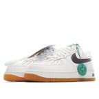 White low-top sneaker with dark swoosh, green tag, and tan gum sole