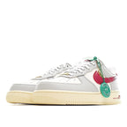 White Air Force 1-style sneakers with red quarter panel, green lace tag, and gum sole