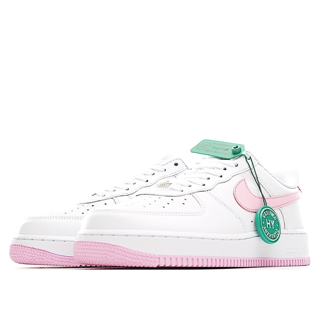 White Nike Air Force 1 sneakers with pink logo, green hang tag, and pink sole