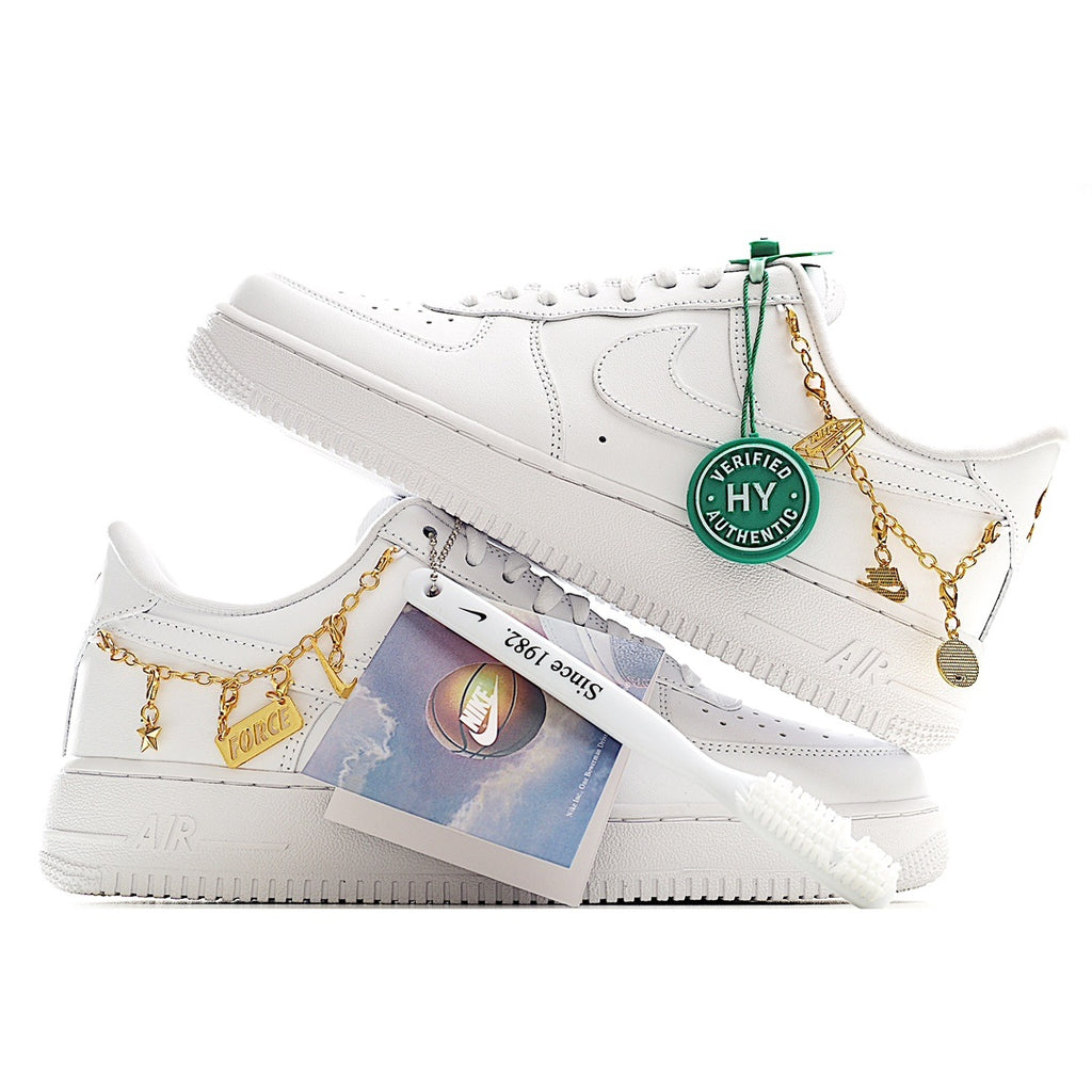 White low-top sneakers with green tag and gold chain charms, front side view