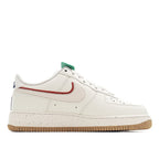 White Nike Air Force 1 sneaker front quarter view with red swoosh, green lace tag, gum sole