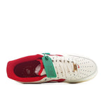 Low-top sneakers with white leather, red lining, and green-and-red tag on laces