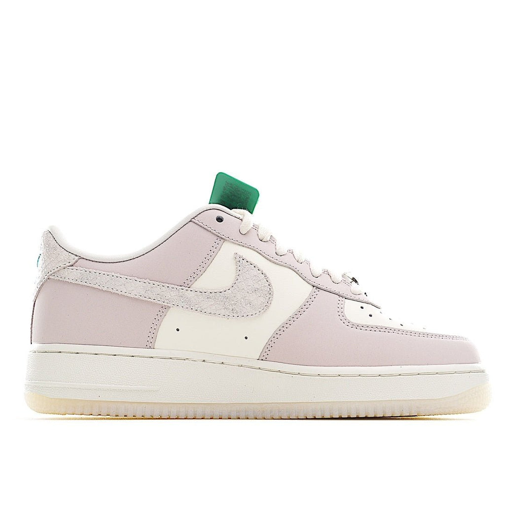 Low-top sneaker side view in pale pink and white with green heel detail.