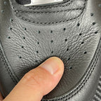 Sneaker toe with black leather texture, perforated eyelets, and stitched trim