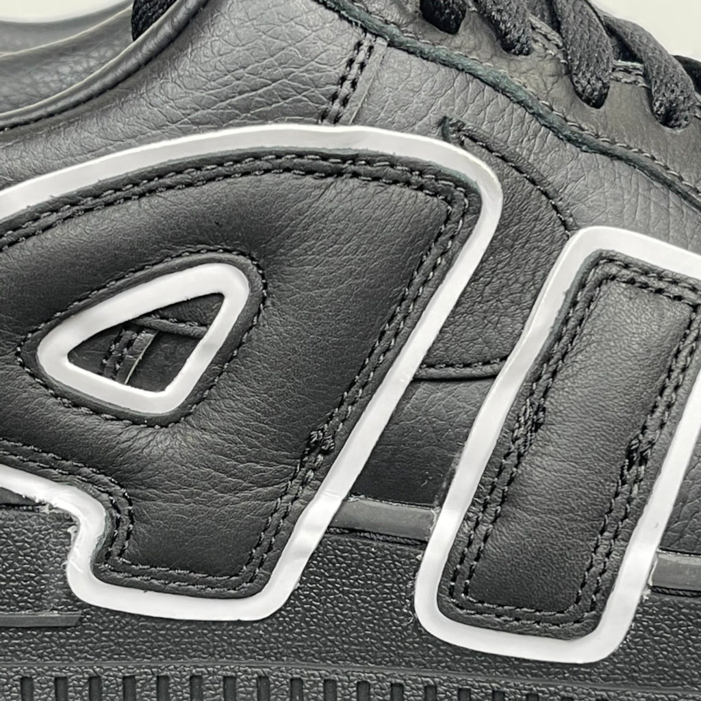 Black sneaker quarter panel close-up with white U-shaped logo details and stitching.