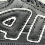 Black sneaker quarter panel close-up with white U-shaped logo details and stitching.