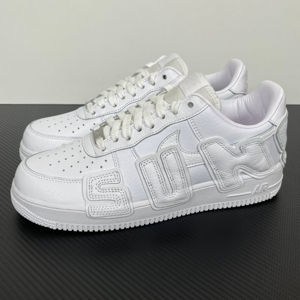 White leather Nike low-top sneakers with lace-up front, perforations, and stitched side panels.