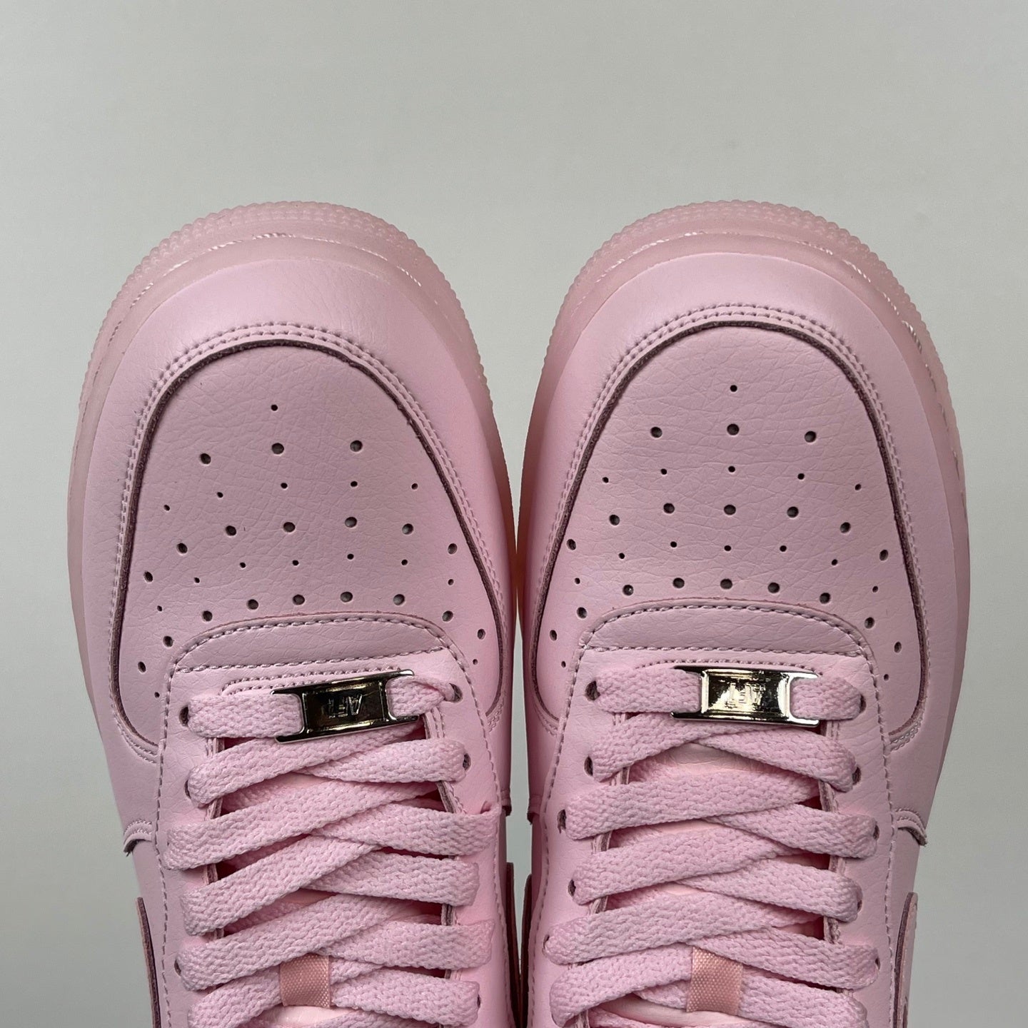 Pink low-top sneakers with perforated toe and two metallic lace eyelets